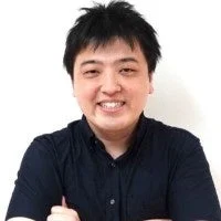 短い黒髪のアジア人男性が、黒いシャツを着て腕を組み、笑顔でカメラを見つめているポートレート