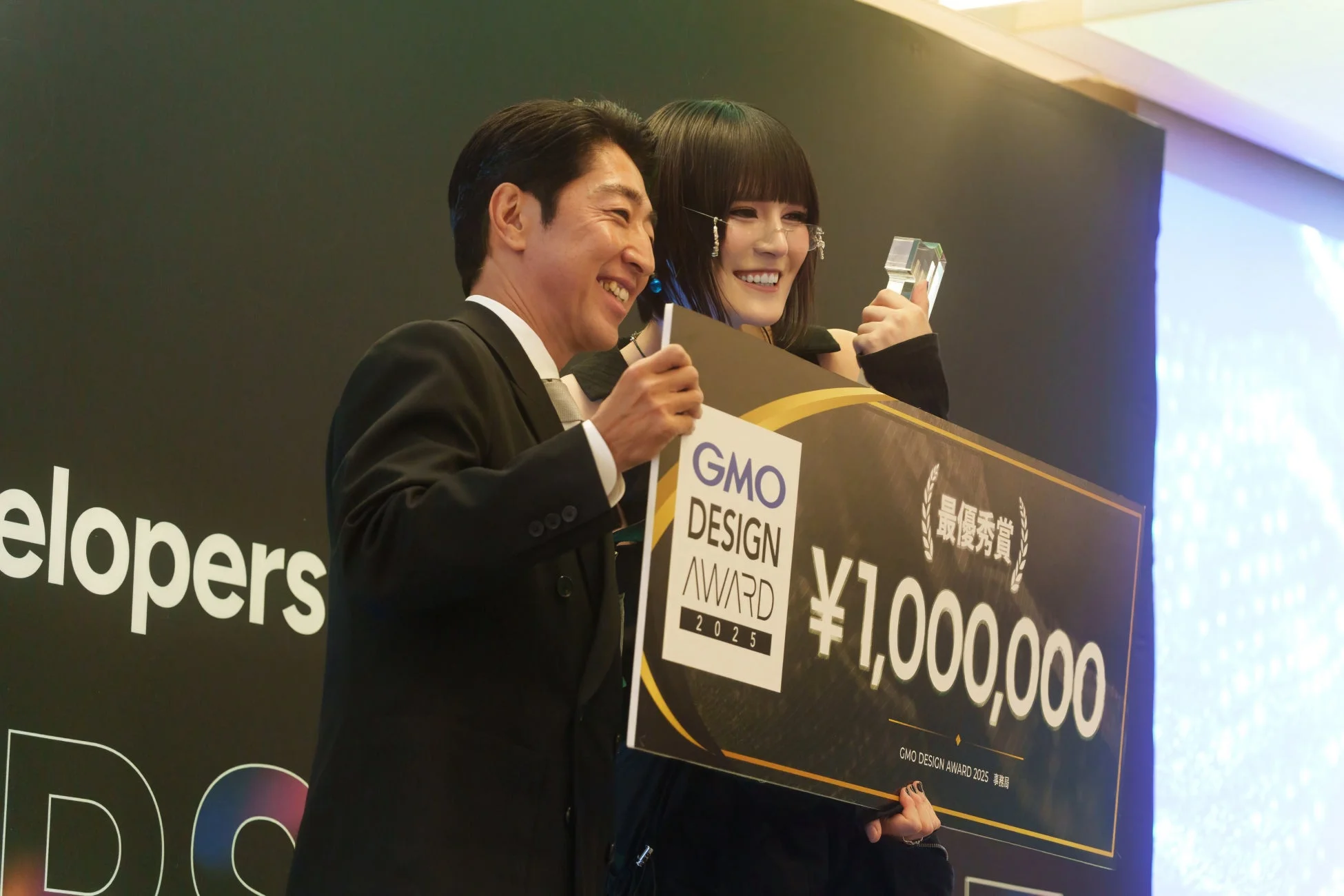 授賞式で最優秀賞と賞金100万円のボード、そしてトロフィーを笑顔で受け取る二人の男女