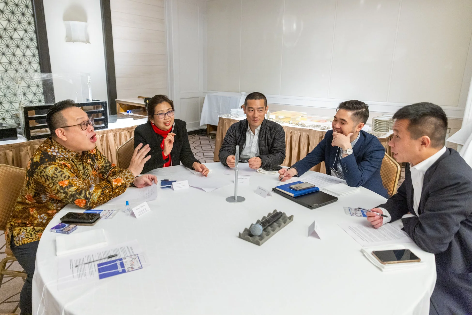 円卓を囲んで5人の男女が活発なビジネスミーティングを行っている様子