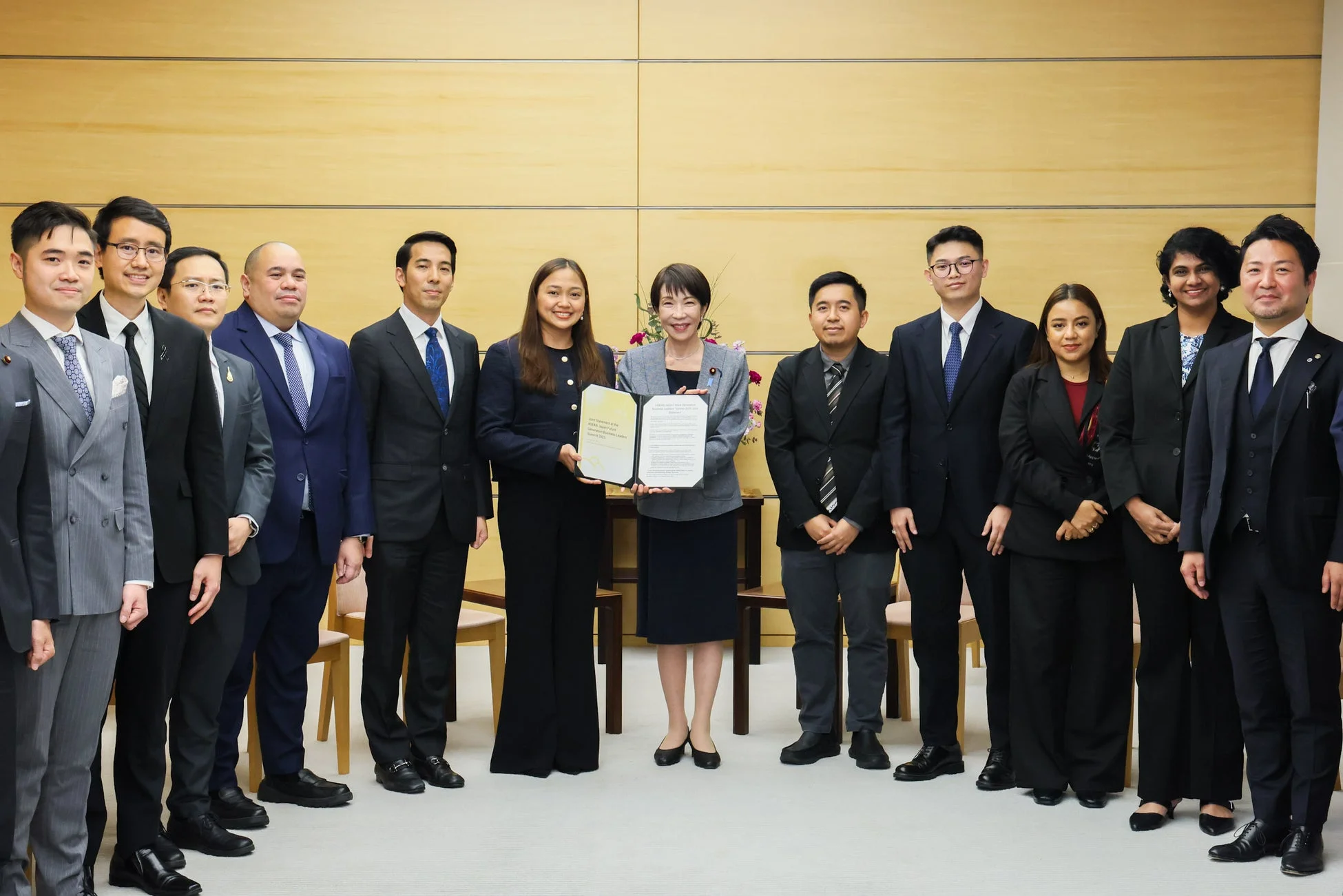 ASEANと日本のビジネスリーダーサミットの共同声明を持つ女性を中心に、多くの関係者が集まった集合写真