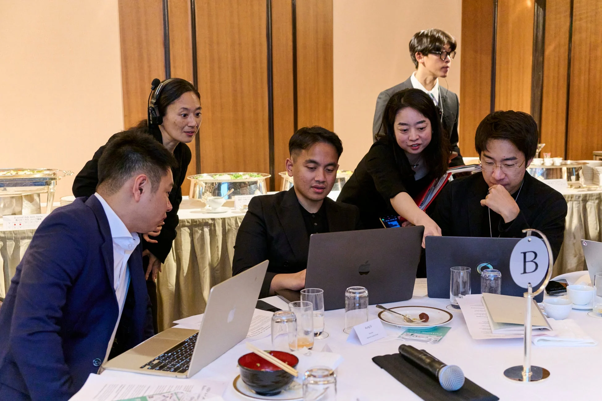 会議室のような場所で、複数のプロフェッショナルがラップトップを使い、活発に議論したり共同作業をしている様子