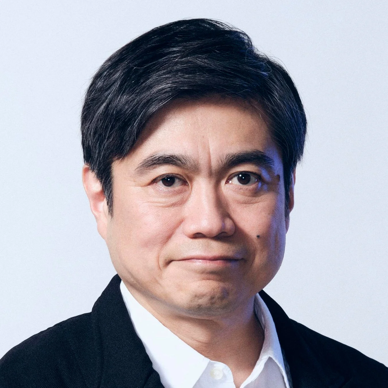 黒いジャケットと白いシャツを着用したアジア系の中年男性のポートレート。男性はカメラをまっすぐ見つめており、落ち着いた真面目な表情をしている。背景はシンプルな白。