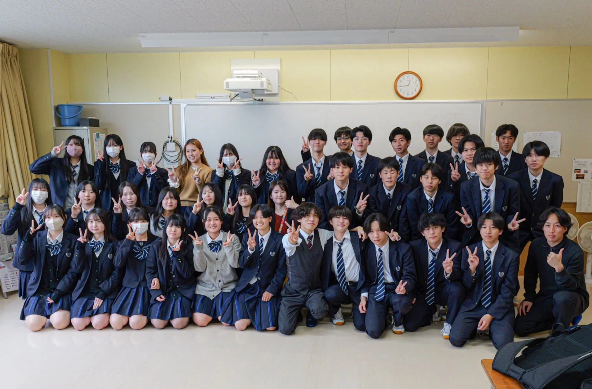 教室で制服を着た大勢の日本の学生が集合写真を撮っています