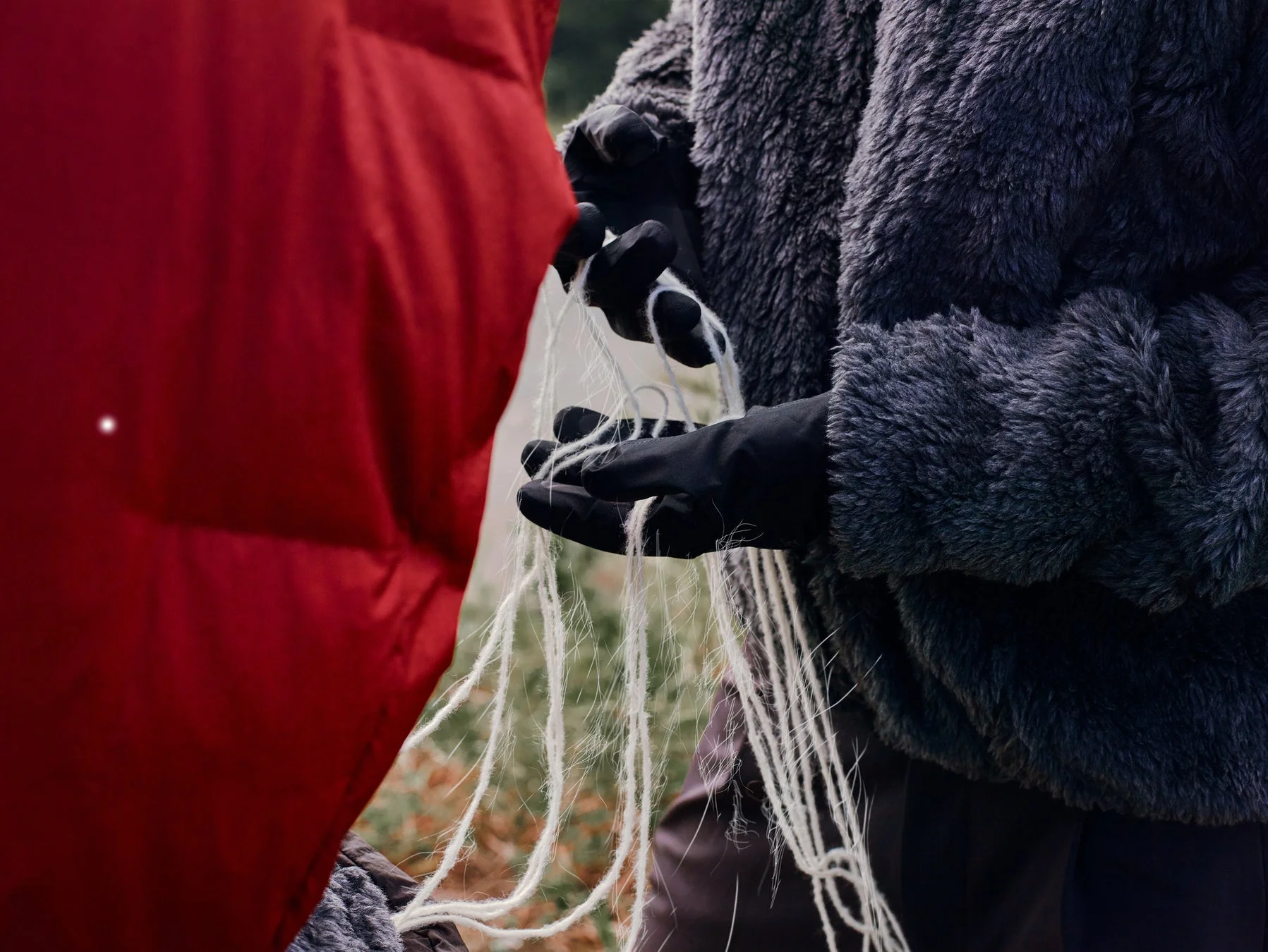 黒い手袋をはめた手が白い糸状のものを操っているクローズアップ