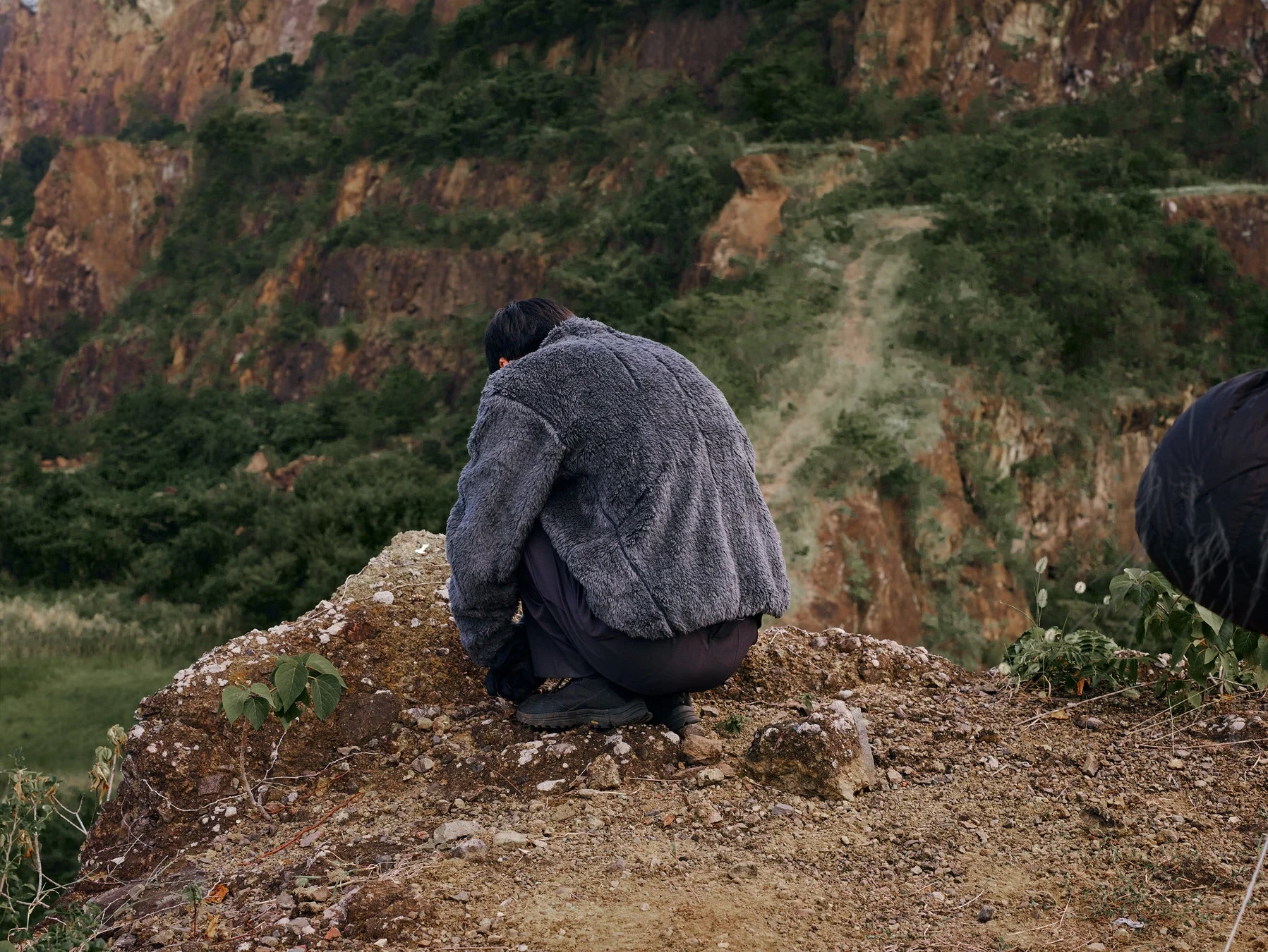 フリースジャケットを着た人物が岩だらけの地面にしゃがみこんでいる