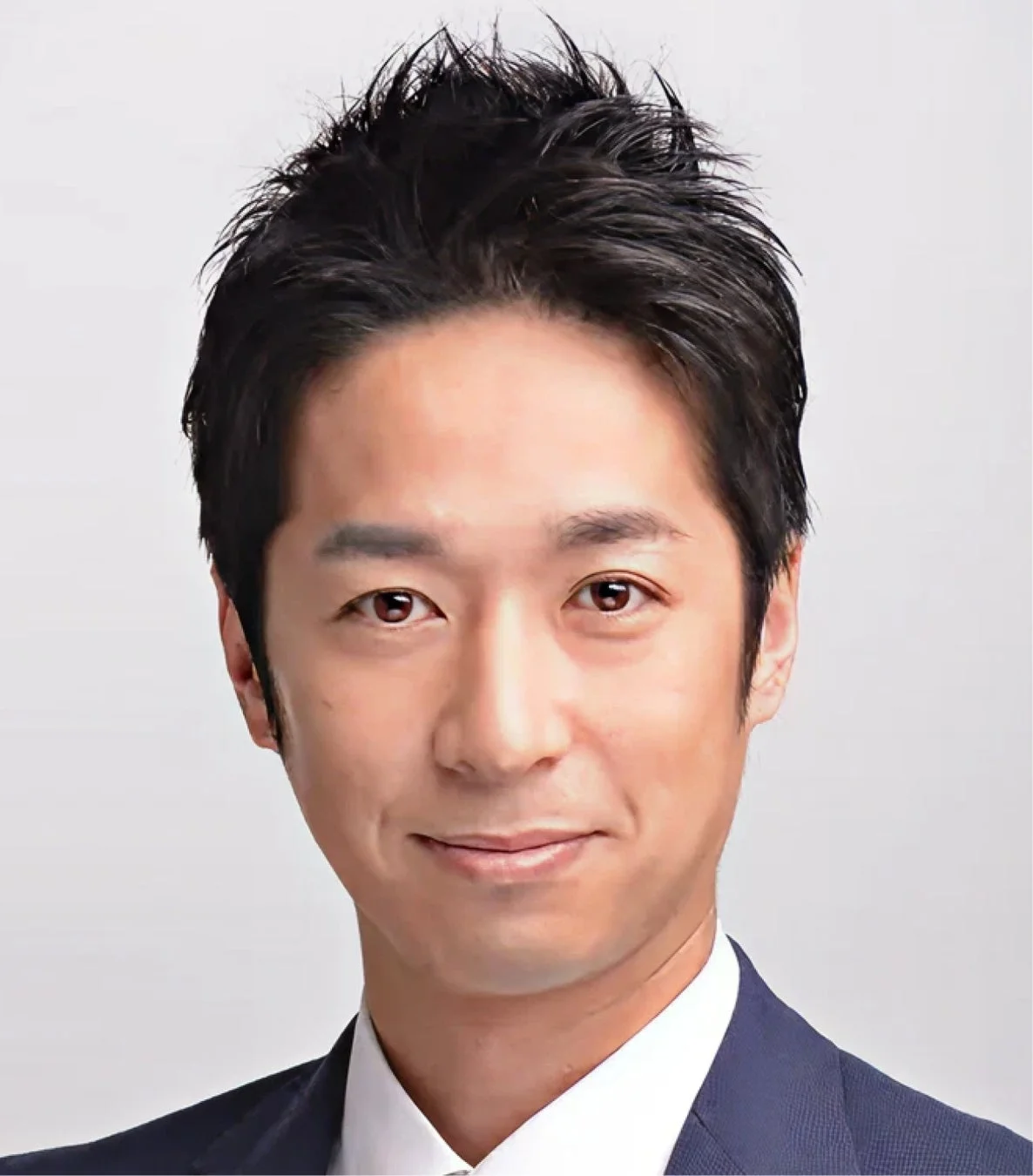 ダークスーツを着用し、白いシャツを着たアジア人男性の顔のアップです。彼は穏やかな笑顔を浮かべ、カメラをまっすぐ見ています。清潔感があり、プロフェッショナルな印象を与えるポートレート写真です。