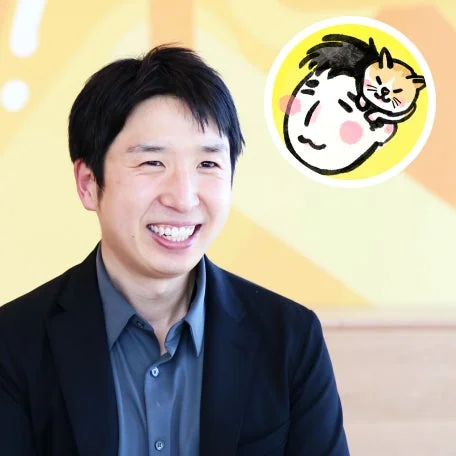笑顔のアジア人男性がビジネスウェアを着用しており、右上には猫と人物のイラストが描かれているポートレート写真