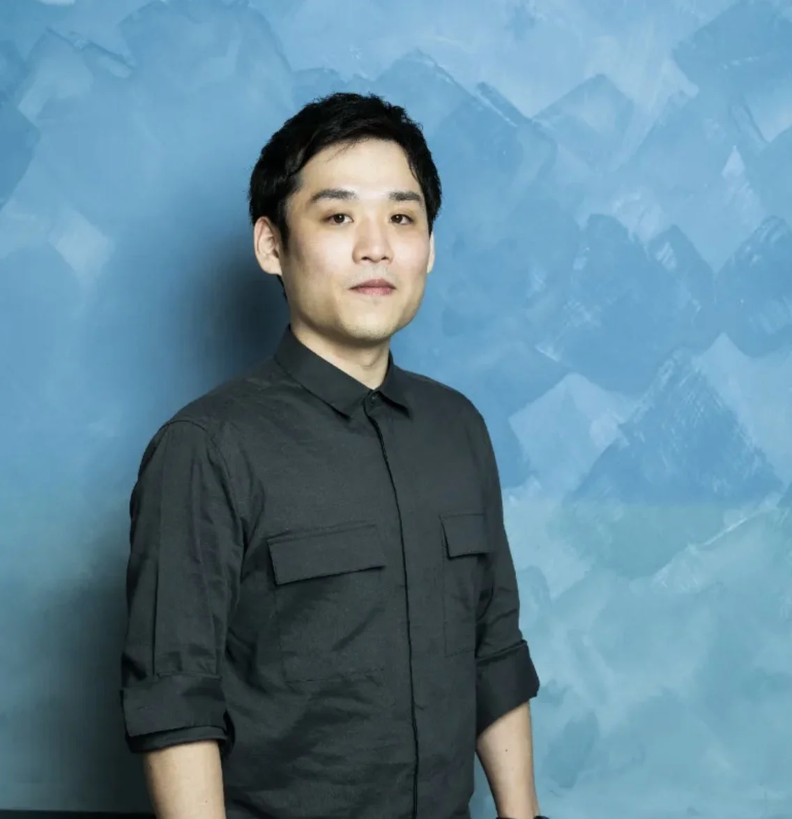 青い模様の壁を背景に、黒いシャツを着たアジア人男性のポートレート