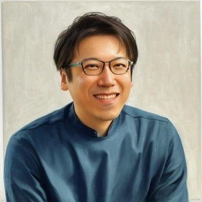 メガネをかけたアジア人男性が笑顔でこちらを見ているポートレート写真