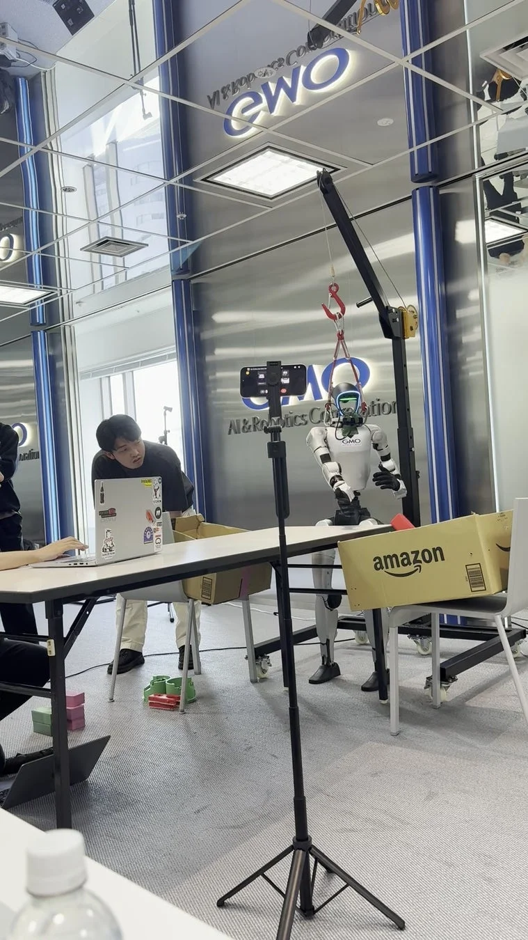 GMO AI & Robotics Co.のオフィスで、ヒューマノイドロボットがAmazonの箱を使った実験を行っています。