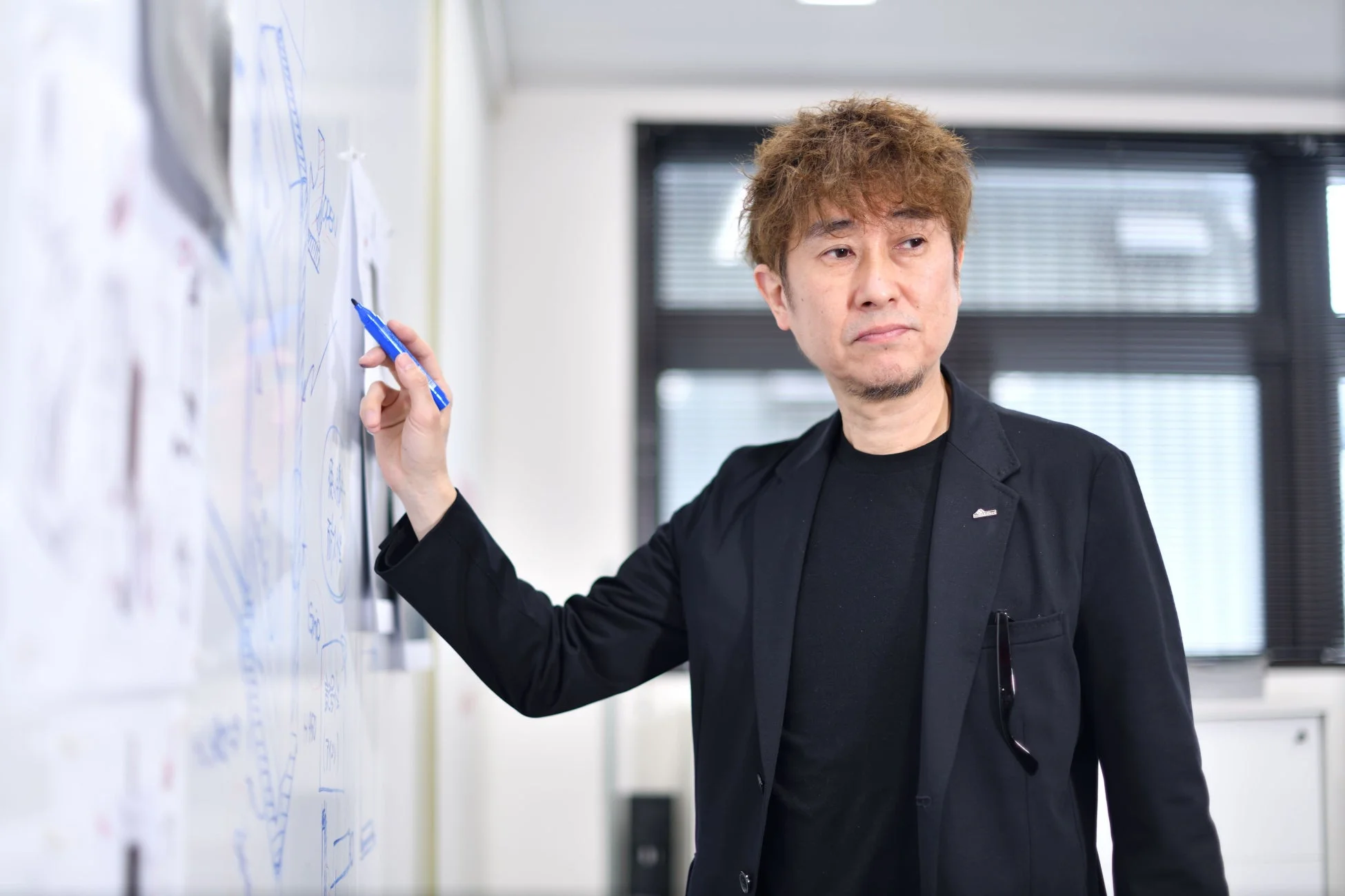 オフィスでホワイトボードに何かを書きながら説明している男性
