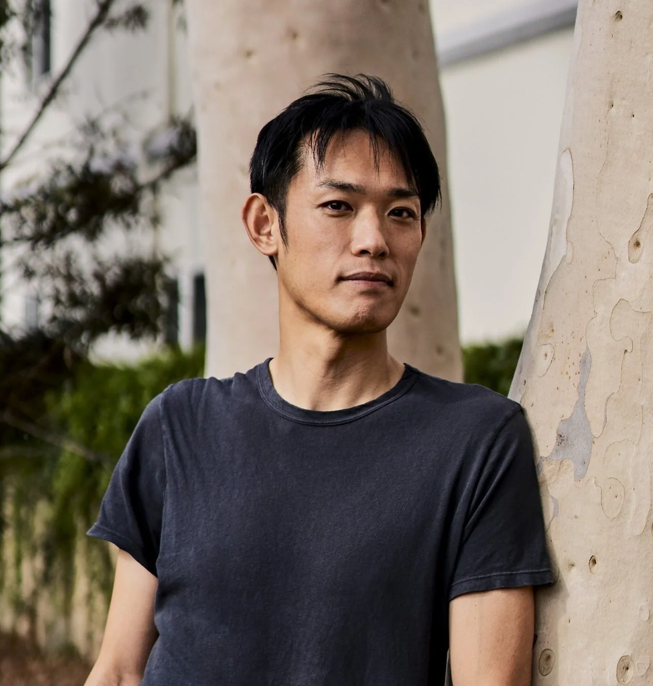 屋外で木に寄りかかっているアジア人男性のポートレート