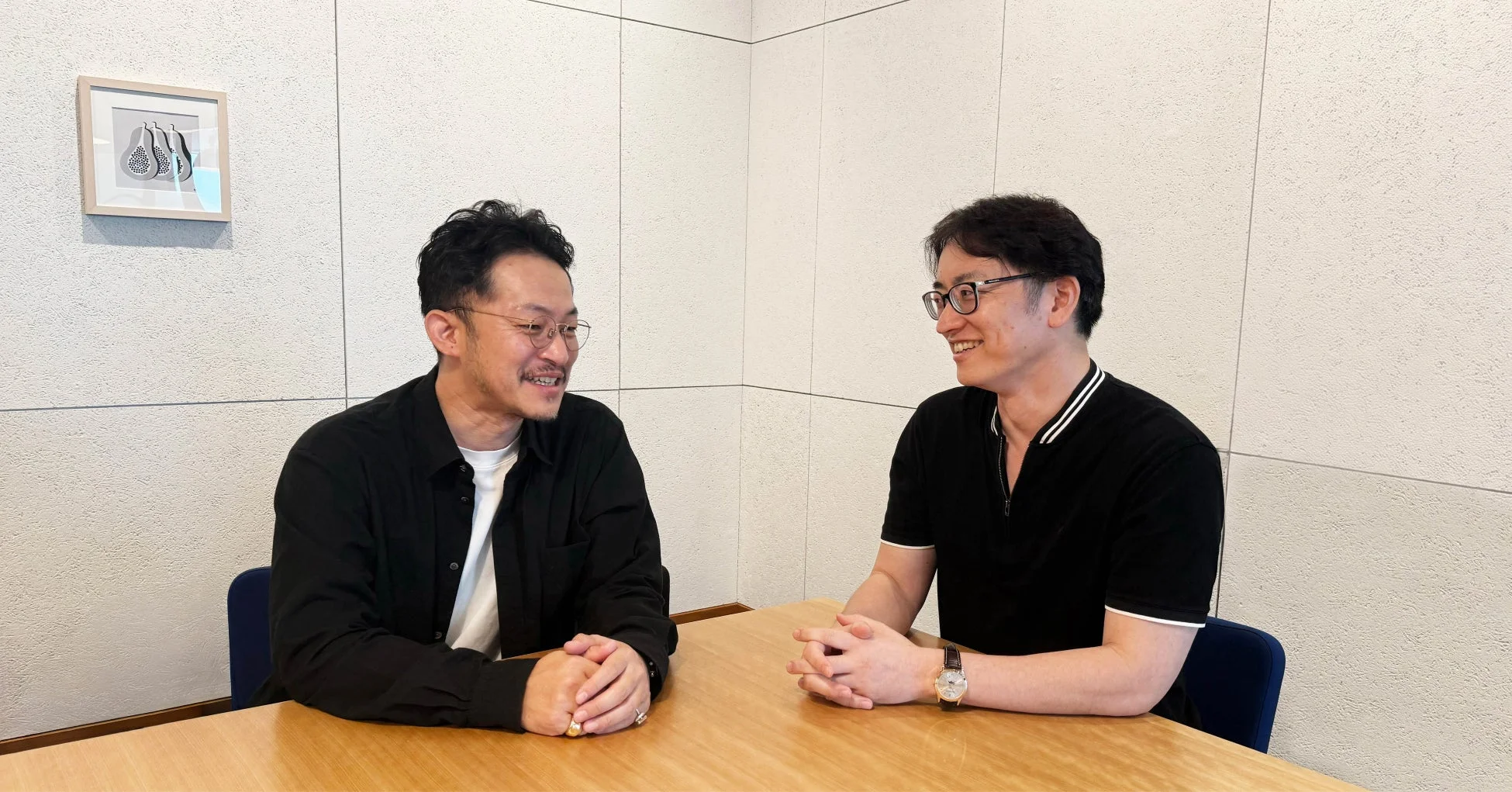 二人の男性がテーブルを挟んで向かい合い、笑顔で会話している様子を捉えた画像です。